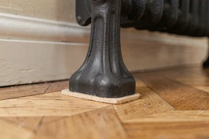 Pied en fonte de radiateur avec protection feutre posé sur un parquet en chêne clair pour éviter les marques